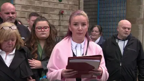 Alexandra Whyte standing outside court with a folder in her hand. She is flanked by several people on either side of her.