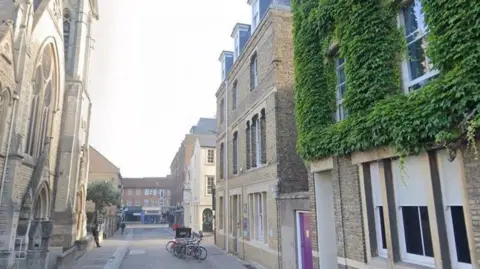 Google Street View image looking along St Michael's Street, with a medieval stone church on the left side and brick terraced houses on the right.