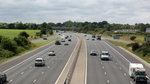 A picture of a dual carriageway with many cars and vans driving.