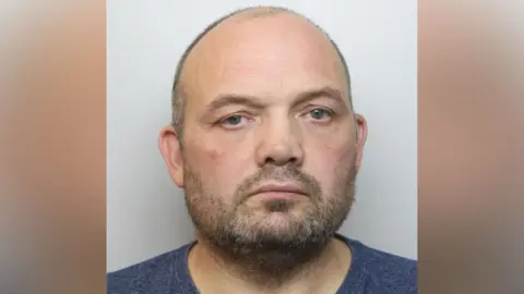 Northamptonshire Police A man with a beard in a navy T-shirt looks directly at the camera.