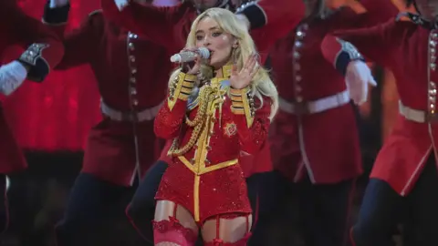 PA Media Sabrina Carpenter performs at the 2025 Brit Awards. She is wearing a military-style red costume with red stockings and suspenders.