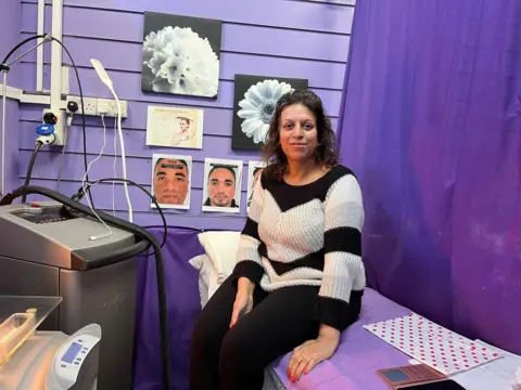 A lady sits on a bed and smiles at the camera