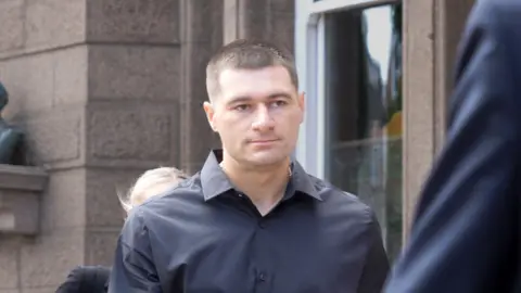 BBC Artur Sevash-Zade wearing a black shirt walks into court. He has short black hair and is clean shaven.