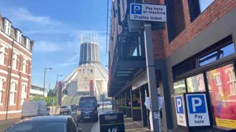 A parking meter in the street in Liverpool. Liverpool Metropolitan Cathedral
 is in the background.