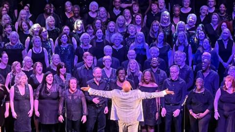 Choir group performing on stage with Gareth Fuller leading the group