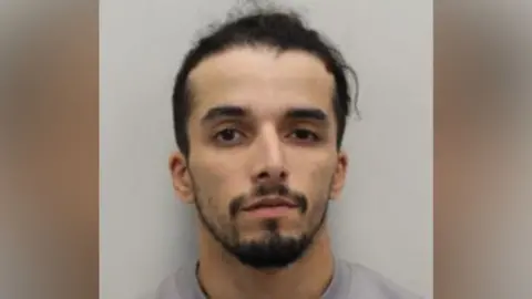 Brahim Kaddour-Cherif wears a grey sweater. He has a beard and moustache