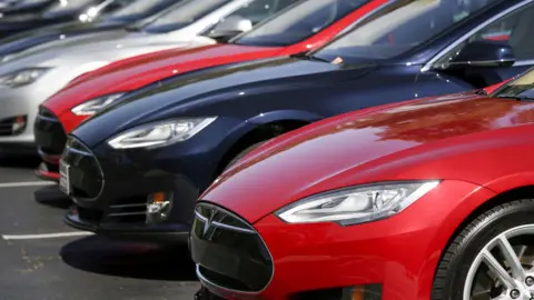 Line of red, black and silver Tesla cars parked in a car park