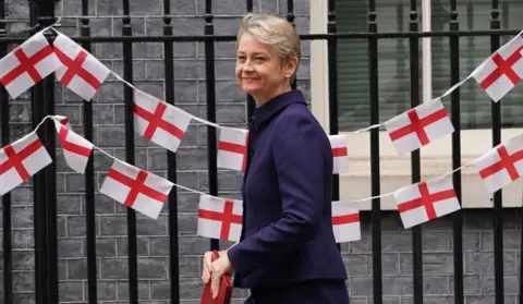 Home Secretary Yvette Cooper arrives at Downing Street in front of a row of English flags