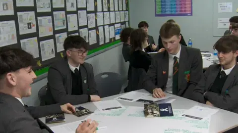 west belfast schoolboys in grey uniform sat around table looking at paperwrk