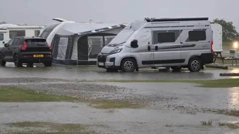 Dornoch Caravan and Camping Park Flooding on a caravan and camp site in Dornoch. There is water covering the ground and cars and caravans parked in the field. 