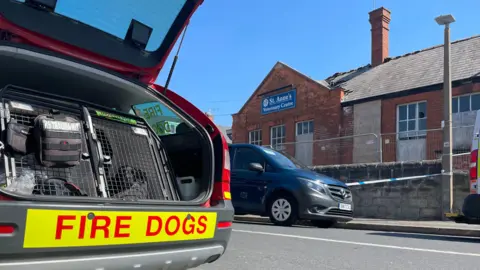 BBC Fire Dogs vehicle parked by a police cordon around a derelict building