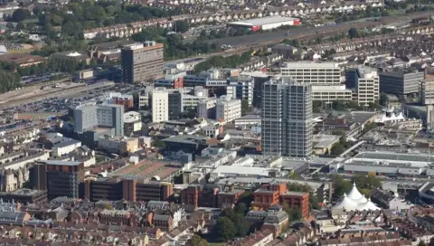 Getty Images Skyline view of Swindon showing various tall buildings, offices and homes with a train station in the distance.