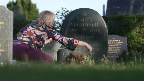 Harris Trust A woman with a flowery blouse crouches with a water in front of a gravestone.