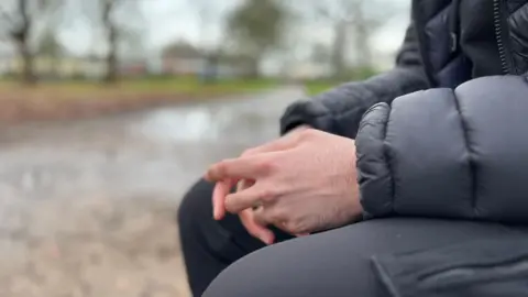 A close up image of Qasim's hands as he sits on a park bench in Clifton