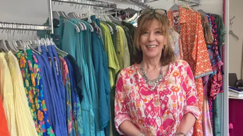 A smartly dressed woman standing in front of rails of clothing in her boutique