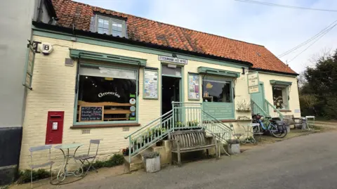 Paul Moseley/BBC The outside of a shop. It is a two-storey building with the brickwork painted in yellow. The wooden adornments are in a light green.