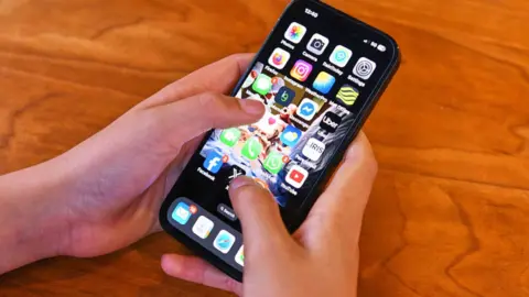 A teenager's hands holding a phone with lots of apps on the screen.