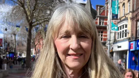 Karen Rowland has blonde and white shoulder-length hair and is standing in Broad Street in Reading.