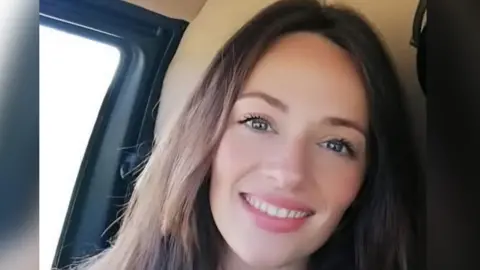 Charlotte Beynon pictured in the front seat of a car smiling at the camera. She has long brown hair 