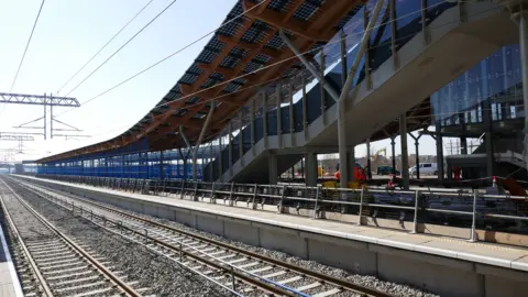 SRSA Colas A view of the new railway station, with tracks, a platform and a footbridge.