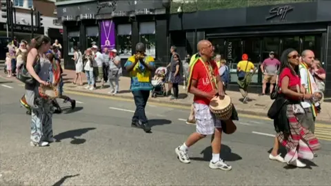A troupe of drummers walking through a town centre as part of a carnival.