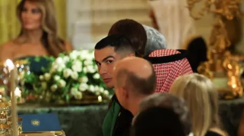 Reuters Christiano Ronaldo looking directly at a camera while attending a lavish state dinner at the White House, with a blurry but recognisable Melania Trump in the background 