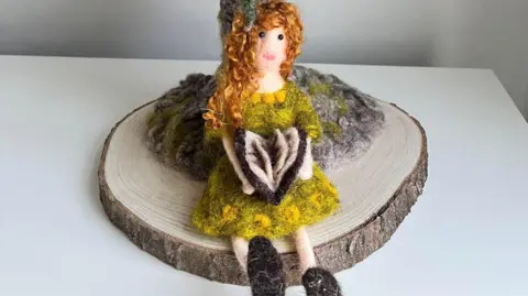 Mandy Smith/needlefeltingnook A needle felted woman sitting under a tree reading a book.