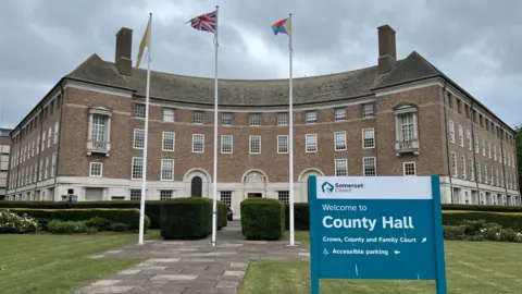 BBC Photo of the outside of County Hall in Somerset including flags and council house sign