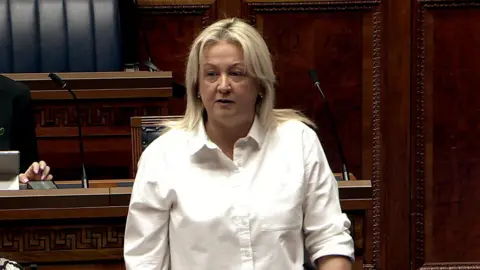 Sinéad Ennis has short blonde hair and is wearing a white shirt. 