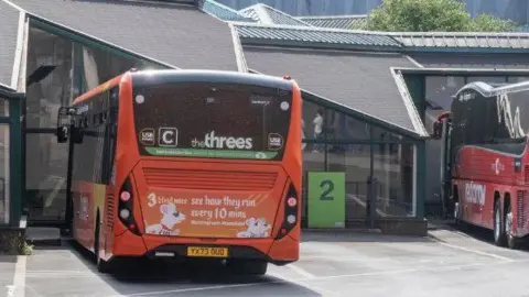 Two buses parked at Victoria Bus Station, a single storey building with glazed walls
