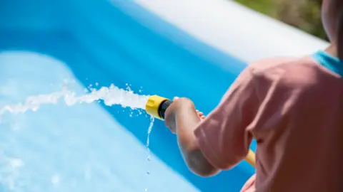 Getty Images A child filling up a paddling pool with a hosepipe.