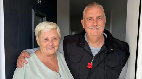 Yvonne is pictured on the left in a blue top with Terry on the right in a black gilet with his hand around Yvonne. 