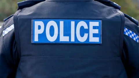UK police officer close-up of the back of a stab vest with the Police logo prominent.