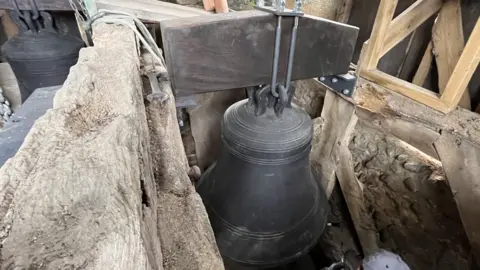 Shaun Whitmore/BBC A dark-coloured church bell suspended between timbers 