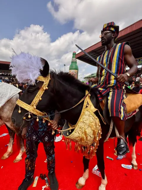 Kyla Herrmannsen / BBC A man on a horse dressed in golden brocade, standing on a red carpet.