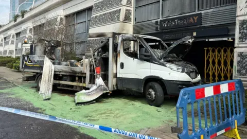 A close up of the truck, which is scorched black outside the car park and there is a piece of police tape cordoning off the area