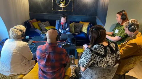 Five voters, three women and two men, sit in a circle around Matt Chorley, who is sitting on a large sofa in front of a laptop and speaking into a red microphone