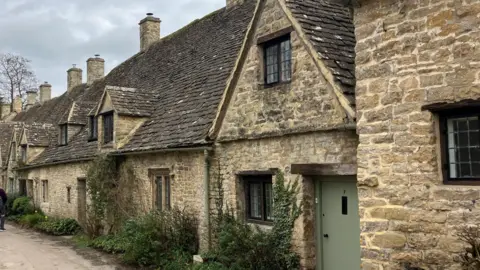 Arlington Row in Bibury - a row of stone cottages with greenery and a stream running in front of them. 