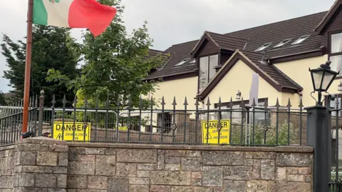 Metal fencing around a house with neon signs saying 'DANGER demolition in progress'