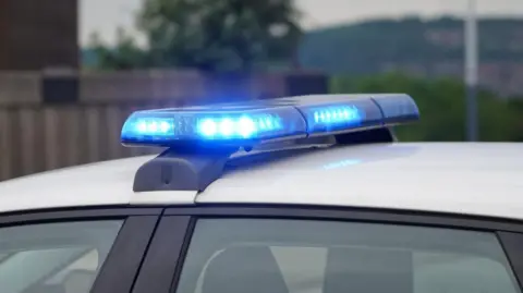 A police car's roof showing a lit up blue light on a white car. 