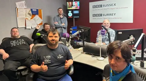 Four people in black t-shirts sit in a radio studio with radio presenter Danny Pike and a support worker 