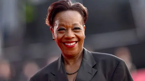 Getty Images Marianne Jean-Baptiste attends the Hard Truths Headline Gala during the 68th BFI London Film Festival at The Royal Festival Hall on October 14, 2024 in London, England. She has short black hair and is smiling. She is waring a grey jacket.