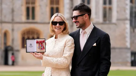 PA Media Carey Mulligan (Carey Mumford) wearing a white dress with husband Marcus Mumford wearing a black suit after being made a Commander of the Order of the British Empire