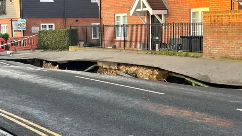 BBC/ADRIAN HARMS Another view of the sinkhole in Godstone High Street. There is a house in the background., as well as a 'For Sale' sign outside another property. 