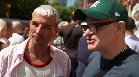 Danny Beard wearing white t-shirt and pink shirt with Jonathan Harvey in a cap, t-shirt and glasses