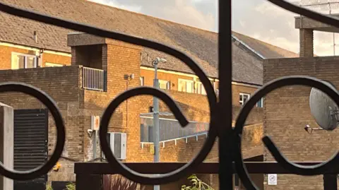 LDRS A CCTV camera mounted on a pole, photographed through a wrought-iron gate.