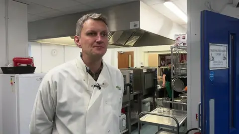 BBC Adam Curtis, of Dolce School Catering in Manchester, stands in a kitchen wearing a white overall