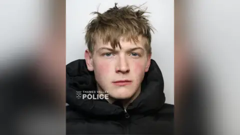 A mugshot of a young man in a black hoodie with a Thames Valley Police logo in the bottom left corner