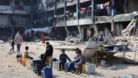 Children sit next to water cans at a school turned shelter in Jabalia, Gaza, on 4 February 2025