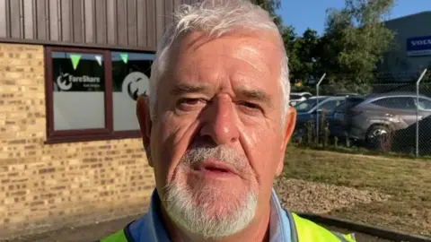 Mike Barrett, wearing a high vis jacket, looking at the camera, he has grey hair and a beard